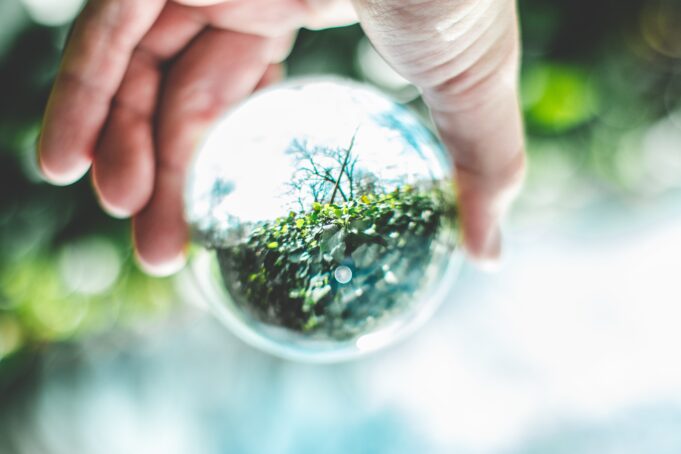 Natur speglas i en glasboll som hålls av en hand. Luonto näkyy lasipallossa, joka on henkilön kädessä.