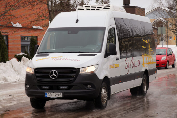 Minibuss med texten ByaBussen kör på en väg. Minibussi jonka päällä lukee ByaBussen ajaa tielä.