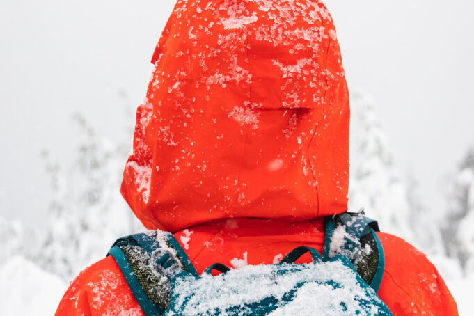 Röd huva och ryggsäck täckt med snö. Lumipeitteinen punainen huppu ja reppu.