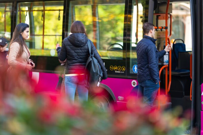 Tre personer framför en rosa buss. Kolme henkilöä pinkin linja-auton edessä.