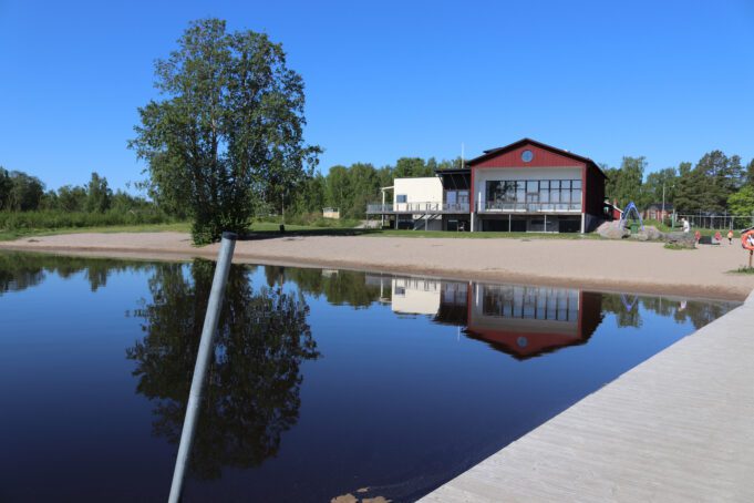 Badstrand med brygga och en paviljong i bakgrunden