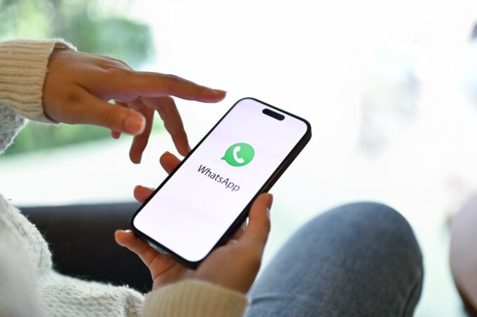 Hand som rör i telefonskärm med en grön Whatsapp-logo.